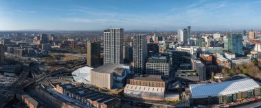 Manchester, İngiltere 'nin hava görüntüsü, modern gökdelenleri, tarihi mimariyi, demiryollarını, beyaz bir çatı binasını ve çevresini gösteriyor..