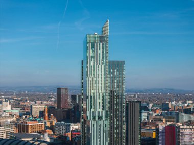 Manchester, İngiltere 'nin hava görüntüsü, çeşitli mimari ve genişleyen kentsel manzara ile çevrili, açısal tasarımlı parlak cam bir gökdelen sergiliyor..