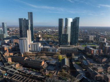 Manchester, İngiltere 'nin hava görüntüsü, Deansgate Meydanı gibi modern gökdelenleri, tarihi tuğla binaları, kanalları ve temiz bir gökyüzü altındaki banliyö bölgelerini gösteriyor..