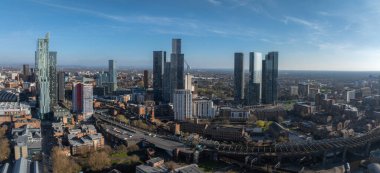Manchester, İngiltere 'nin hava görüntüsü, Deansgate Meydanı kuleleri, modern gökdelenler, tarihi binalar, yollar ve açık mavi gökyüzü altında yeşil alanlar.