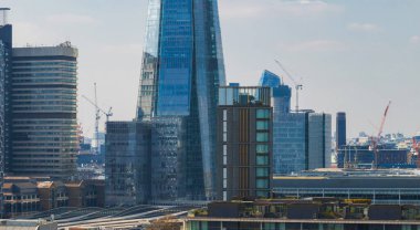Çömlek, modern yüksek binaların, inşaat vinçlerinin ve yeşil çatılı çatıların arasında dimdik duruyor. Londra 'nın gelişen şehir manzarasını parlak bir gökyüzü altında sergiliyor..
