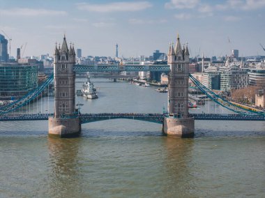 Kule Köprüsü 'nün ikonik kuleleri ve mavi süspansiyon elementleri Thames Nehri boyunca uzanır; arkada HMS Belfast, BT Kulesi ve Londra' nın silüeti bulunur..