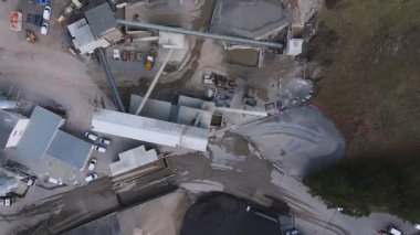 Alplerdeki aktif bir maden alanının hava görüntüsü, dağlık bir arazide makine, araç, taşıma bandı ve malzeme yığınlarını gösteriyor..