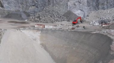 Alplerdeki bir maden sahası, hareket halindeki kırmızı bir kazıcıyı, engebeli araziyi, dik uçurumları ve taş ocağından geçen dolambaçlı toprak yolu gösteriyor..