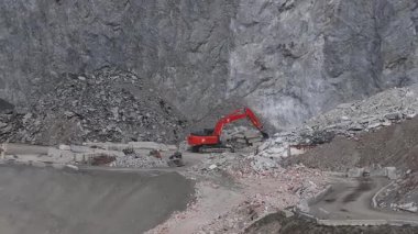 Alplerdeki bir maden alanının havadan görüntüsü, turuncu bir kazıcının kaya kırdığını, enkaz yığınları yarattığını ve dik kayalıkların arasında işlediğini gösteriyor..