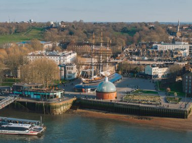 Greenwich, Londra 'nın hava manzarası, Cutty Sark, cam kubbeli tünel girişi, modern nehir kenarı binaları, ve Thames yakınlarında yeşil alanlar.