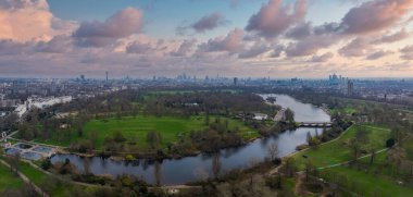 Hyde Park 'ın yeşil alanları ve Serpentine Gölü' nün havadan perspektifi. Arka planda Çömlek ve BT Kulesi de dahil olmak üzere Londra 'nın ufuk çizgisi var..