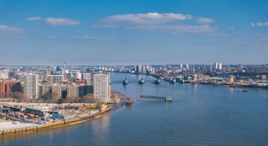 Thames Nehri, Thames Bariyeri, nehir kıyısı boyunca modern binalar ve dağınık bulutlu berrak bir gökyüzü içeren Londra 'nın hava perspektifi.