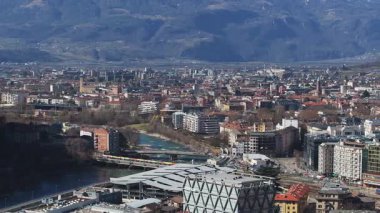 Modern ve geleneksel mimari, inşaat vinçleri, engebeli dağlar ve açık mavi gökyüzünün yer aldığı Bolzano, İtalya 'nın havadan görünüşü.