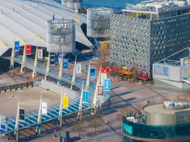 O2 Arenas beyaz kubbesi ve direkleri modern binalarla çevrili, pankartlı bir yürüyüş yolu ve arkada Thames nehri var..