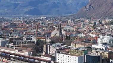 Bolzano, İtalya 'nın havadan görünüşü, hareket halindeki trenleri, canlı mimarisi ve arka planda Dolomite dağları olan bir tren istasyonu..