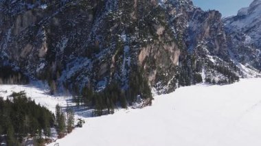 Braies Gölü üzerinde yavaş bir tava, donmuş ve kar kaplı, kayalık uçurumlar ve yoğun yeşil ormanlarla çevrili dramatik bir alp ortamında.
