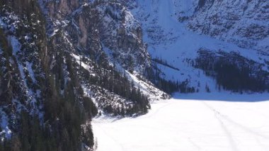 Kuzey İtalya 'daki Braies Gölü' nün havadan görünüşü, donmuş ve karla kaplı, yüzeyinde izler var. Karlı kayalıklar ve gölün etrafını çevreleyen yeşil ormanlar.