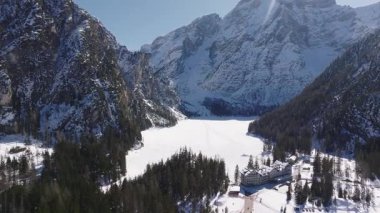 Braies Gölü 'nün kışın donmuş havadan görünüşü, karla kaplı dağlar ve dağlık alandaki ağaçların arasına yerleşmiş binalarla çevrili..