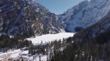 Kış mevsiminde Braies Gölü 'nün havadan görünüşü, donmuş yüzeyi, engebeli kar tozlu dağları, sık yeşil ormanı ve yakındaki araçları olan bir pansiyon..