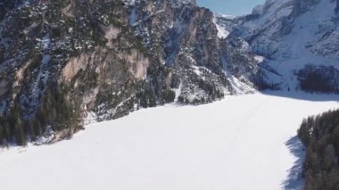 Braies Gölü 'nün donmuş ve karla kaplı havadan görünüşü karlı zirveler ve her zaman yeşil olan ormanlarla çevrili, buzun üzerinde insanlar görünüyor..