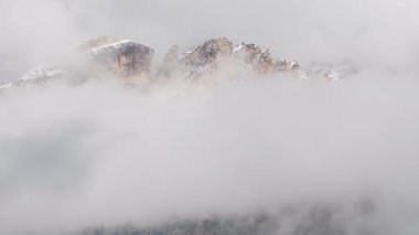 Dolomite dağlarının kar tozlu tepeleri değişen bulutların arasından yükseliyor. Kamera yavaşça süpürüyor, engebeli araziyi ortaya çıkarıyor..
