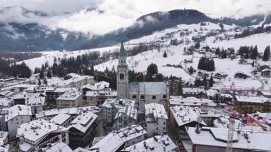 İkonik çan kulesiyle Cortina d 'Ampezzo' nun hava manzarası, karla kaplı çatıları, dağlık binaları ve kışın sisli Dolomite dağ yamaçları..