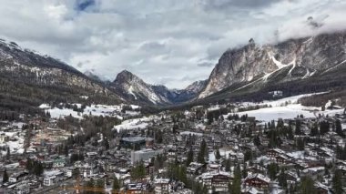 Karla kaplı çatıları, dağlık sokakları, ormanları ve kışın dramatik Dolomite zirvelerini gösteren yavaş, silip süpüren bir Cortina d 'Ampezzo tavası..