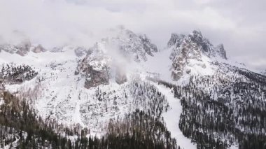 Cortina yakınlarındaki sivri Dolomite tepelerinin havadan görünüşü kısmen bulutlarla örtülü, karlı yamaçlarda daima yeşil ormanlar ve yumuşak kamera hareketleri var..