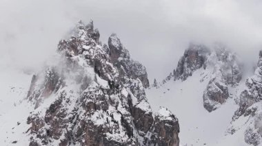 Uçsuz bucaksız, karla kaplı Dolomite tepeleri Cortina yakınlarında, sis ve bulutlar uçurumların ve dağınık yeşil ağaçların üzerinde sürükleniyor..