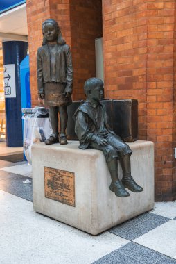 Ayakta duran bir kızın bronz heykeli ve taş bir heykel üzerinde bavuluyla oturan bir çocuk, Londra 'daki Liverpool istasyonunda kırmızı tuğladan bir duvara dayanıyor..