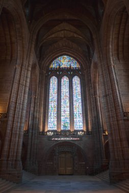 Liverpool Katedrali 'nin içi kemerli taş sütunlarla çerçevelenmiş ve altında neon ışığı ve Gotik Uyanış detayları olan büyük boyalı bir pencereyi ön plana çıkarıyor..