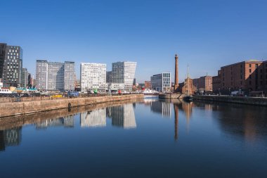 Liverpool 'un Albert Rıhtımı' nda kırmızı tuğla depoları, Pump House bacası, modern cam binalar ve sakin su yansımaları görülüyor..