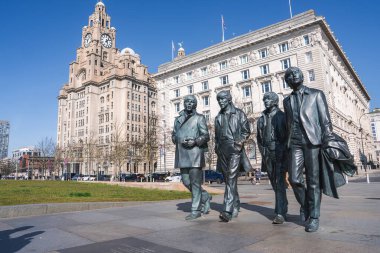 İngiltere 'nin Liverpool kentindeki Royal Liver Binası yakınlarındaki Beatles' ın bronz heykelleri, açık mavi gökyüzü ve tarihi deniz manzarası ile.