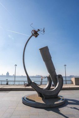 Mersey Nehri ve Liverpool ufuk çizgisine uzanan, üzerinde küçük bir figür bulunan büyük boyutlu bir teleskopun tuhaf bir heykeli, açık mavi gökyüzünün altında..