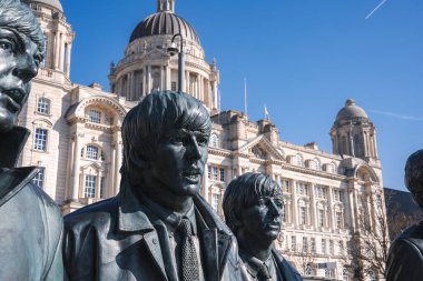 The Beatles 'ın bronz heykelleri Liverpool, İngiltere' de duruyor. Liverpool Limanı 'nın kubbeleri ve açık mavi gökyüzü altında süslü mimarisi var..