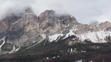 Cortina yakınlarındaki uçsuz bucaksız Dolomite tepeleri bulutlu, aydınlık ve gölgeli. Kamera sarp kayalıkların ve orman yamaçlarının üzerinde süzülüyor..