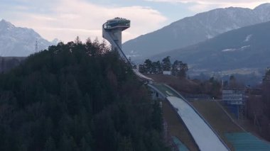 Avusturya 'nın Innsbruck kentindeki Bergisel Kayak Atlayışı' nın kar kaplı Alpler, orman tepeleri ve açık arazilerle hava görüntüsü. Kamera dönüm noktasında sorunsuzca hareket eder..
