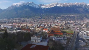 Innsbruck, Avusturya 'nın hava manzarası, Nordkette dağlarını, renkli binaları, tren istasyonlarını, hareket eden araçları ve içinden akan bir nehri gösteriyor..