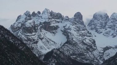İtalya, Dolomitler 'deki karlı dağ zirveleri kısmen bulutlarla kaplı. Donmuş bir göl, bulutların yavaşça üzerimizden kaymasıyla manzarayı yansıtır..