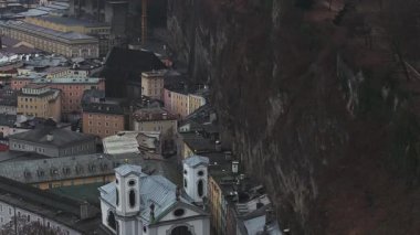 Hohensalzburg Kalesi, şehir mimarisi, ağaçlık tepeler ve bulutlu gökyüzü altındaki uzak dağların yer aldığı Salzburg, Avusturya 'nın hava manzarası..