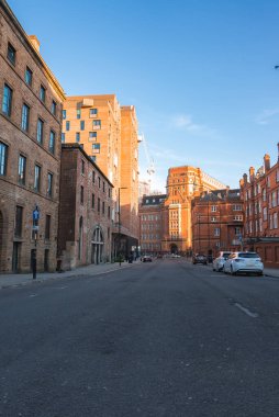 Tarihi kırmızı tuğla ve modern binaların yer aldığı Manchester, İngiltere 'de sessiz bir cadde. Bir vinç ve park edilmiş arabalar kentsel gelişimi vurguluyor.