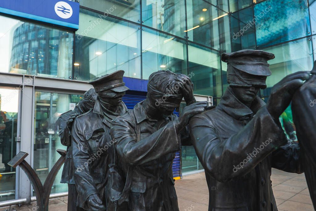 Bronze sculpture of seven blindfolded soldiers near Manchester Piccadilly Station, with a modern glass building and British Rail logo in the background.