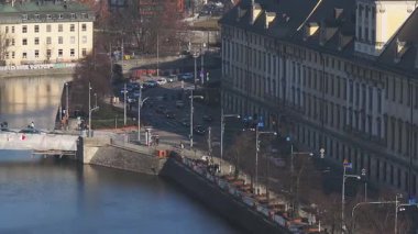 Wroclaw, Polonya 'da hareket halindeki araba ve yayaların olduğu bir köprünün havadan görüntüsü. Nehir yakınlardaki binaları, ağaçları ve ziyaretçilerin olduğu bir parkı yansıtıyor..