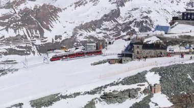 İsviçre, Zermatt yakınlarındaki Gornergrat gözlemevinin hava manzarası, Matterhorn, istasyonda kırmızı bir tren ve karlı bir arazide turistler..