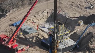 İşçiler, kırmızı vinç ve sondaj kulesi de dahil olmak üzere, görünür hareket ve aktif saha çalışmalarına sahip güçlendirilmiş beton bir yapı üzerinde ağır makineler kullanıyorlar..