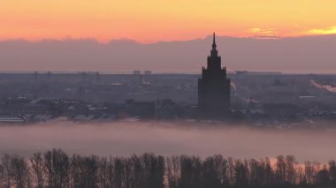 Riga, Letonya 'da sakin bir sabah, puslu çatılar, Letonya Bilimler Akademisi ve turuncu bir güneşin altında Daugava Nehri. Duman hareket katar.