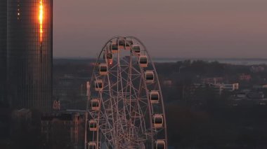 Riga 'nın dingin sabah manzarası. Dönme dolap, modern binalar, vinçler ve ağaçlar, gündoğumu renkleri ve soluk sabah sisi..