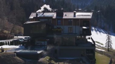 Güney Tyrol, İtalya 'da modern bir otel. Arkasında tahta kirişler, cam pencereler ve Dolomite dağları var. Bacalardan duman yükseliyor..