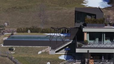 Güney Tyrol, İtalya 'da cam kenarlı sonsuz havuzu, modern güvertesi, çimenli yamacı ve uzaktan kumlu dağları olan bir otelin havadan görünüşü..