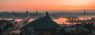 Riga, Letonya 'nın sabah manzarası, Ulusal Kütüphane, tarihi kilise kuleleri, Daugava Nehri ve yumuşak sisli kemerli demiryolu köprüsü..