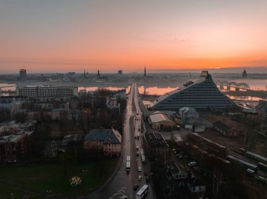 Riga, Letonya 'nın sabah manzarası, Ulusal Kütüphane, Daugava Nehri, tarihi kilise kuleleri, demiryolu köprüsü ve hareketli kentsel caddeler.