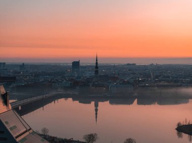 Riga, Letonya üzerinde sakin bir gün doğumu, Aziz Peter Kilisesi kulesi, tarihi binalar ve modern yapılar Daugava Nehri 'ne yansıyor..