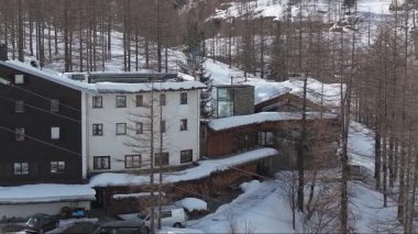 Karlı Dolomitler 'de lüks bir otelin havadan görünüşü, Alp mimarisi, bir duvar resmi, bir kayak asansörü, ve park halindeki araçlarla sakin bir kış manzarası..