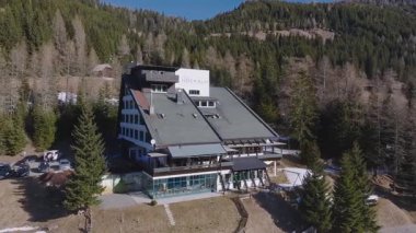Dolomitlerdeki Nockalm Oteli 'nin etrafını çevreleyen hava manzarası, etrafını çevreleyen yemyeşil ağaçlar, çıplak ağaçlar, kar bantları ve dağ evi tarzı binalarla çevrili..